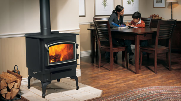 black wood stove with fire burning in a room. woman and child sitting at a table in the background