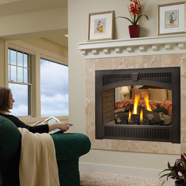 black fireplace insert with fire burning in it. White hearth above it with painting on it. Woman sitting on green couch reading