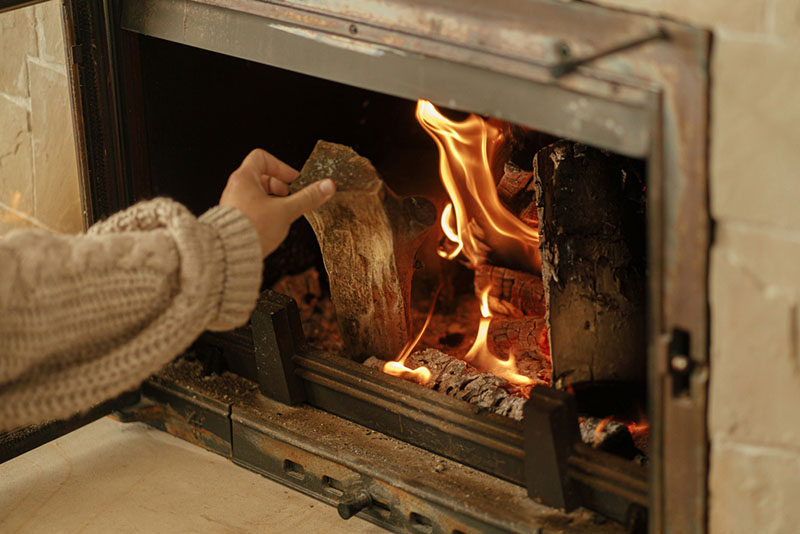 A woman putting wood into a lit fireplace 