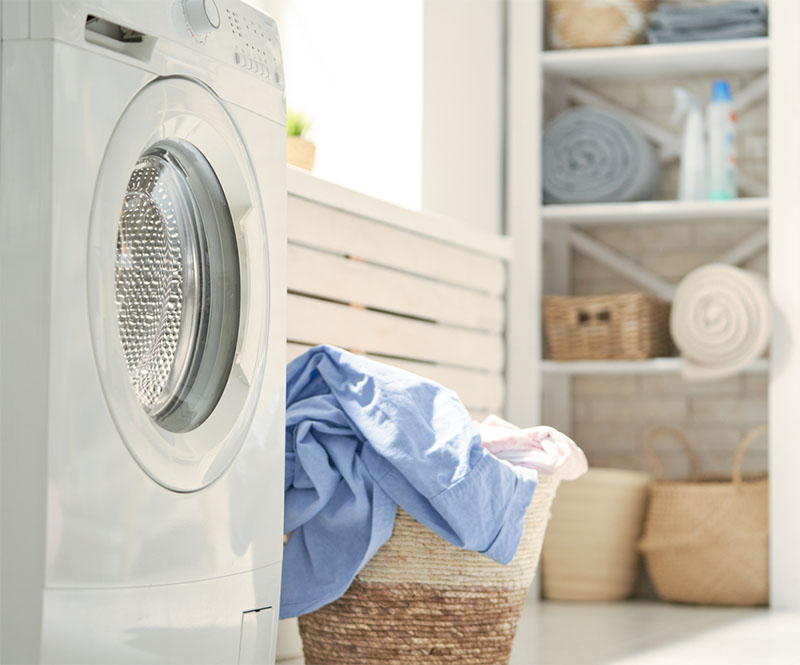 A white dryer inside a laundry room next to a basket of clothes