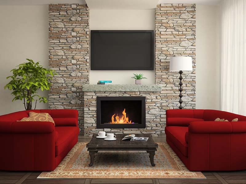 A modern living room with 2 red couches and a lit fireplace with a stone surround